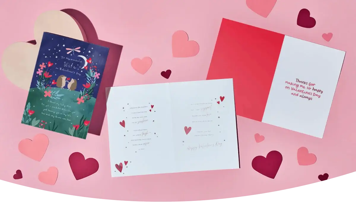 A flat‑lay of Valentine’s Day greeting cards on a pink background, surrounded by scattered paper hearts in various shades of pink and red.