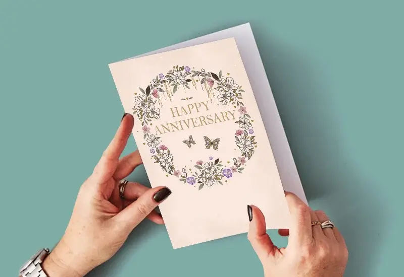 A person holding an anniversary card with a floral wreath design and gold 
