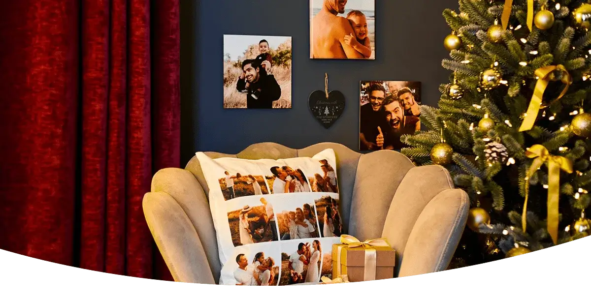 A cozy living room decorated for Christmas with a beige armchair featuring a photo collage pillow, a dark wall displaying several photo prints, and a Christmas tree adorned with gold ornaments and ribbons next to red curtains. A cozy living room decorated for Christmas with a beige armchair featuring a photo collage pillow, a dark wall displaying several photo prints, and a Christmas tree adorned with gold ornaments and ribbons next to red curtains.
