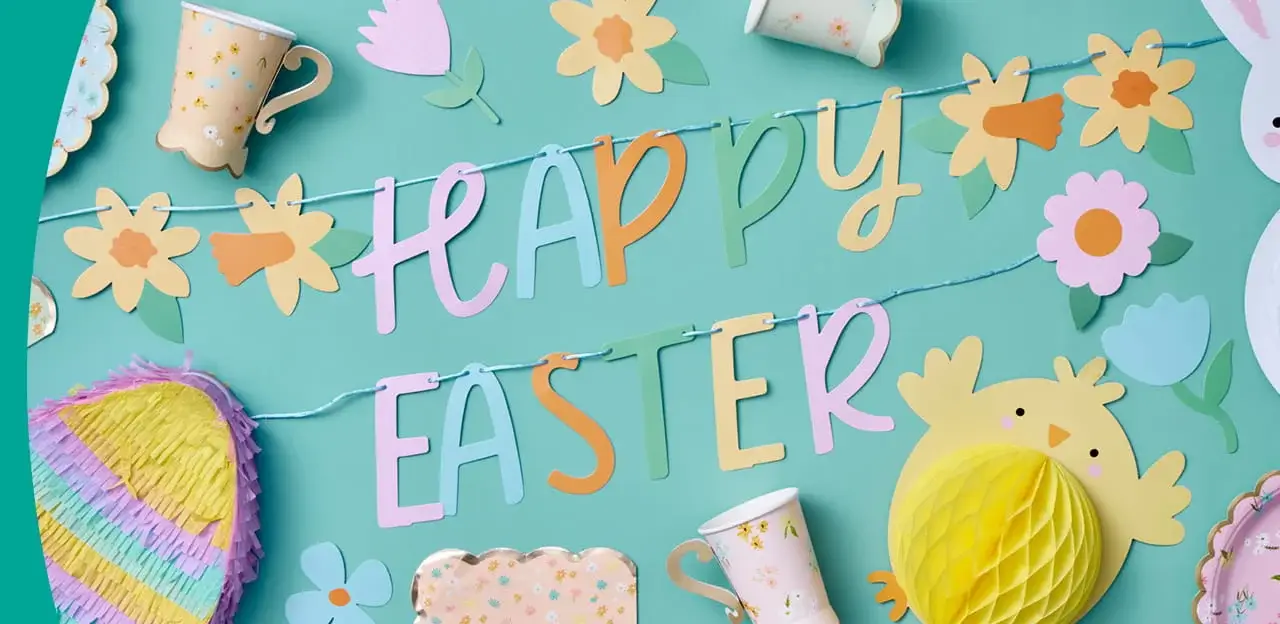 Colourful Easter decorations arranged on a teal background, featuring a Happy Easter banner, floral cut-outs, paper cups and a yellow chick decoration.