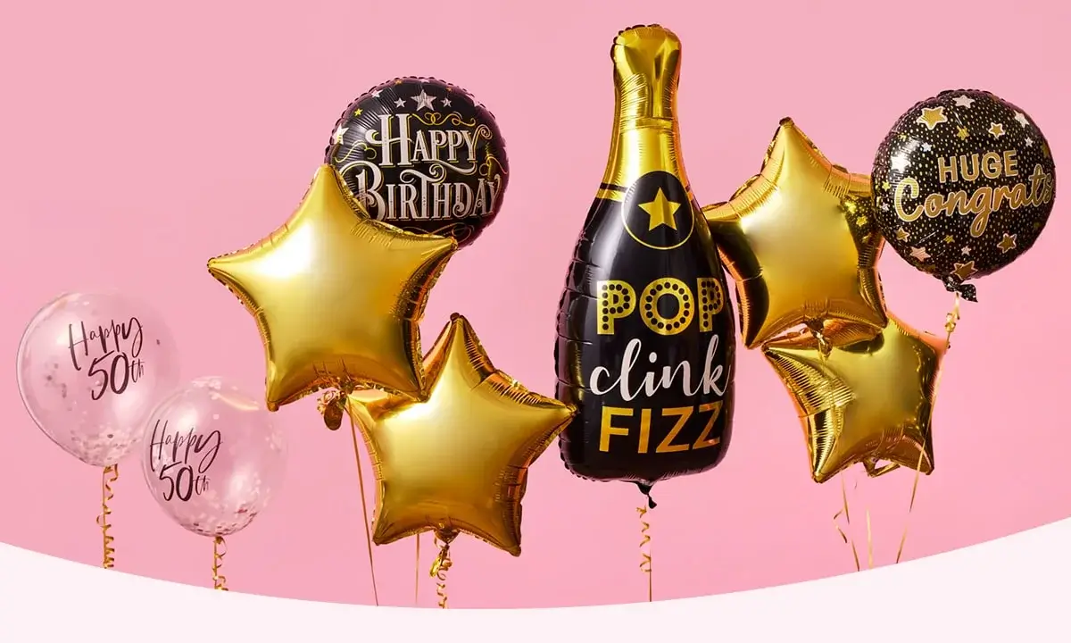 A group of celebratory balloons on a pink background, including gold stars, 'Happy 50th' balloons, and a champagne bottle-shaped balloon with the text 'POP clink FIZZ'