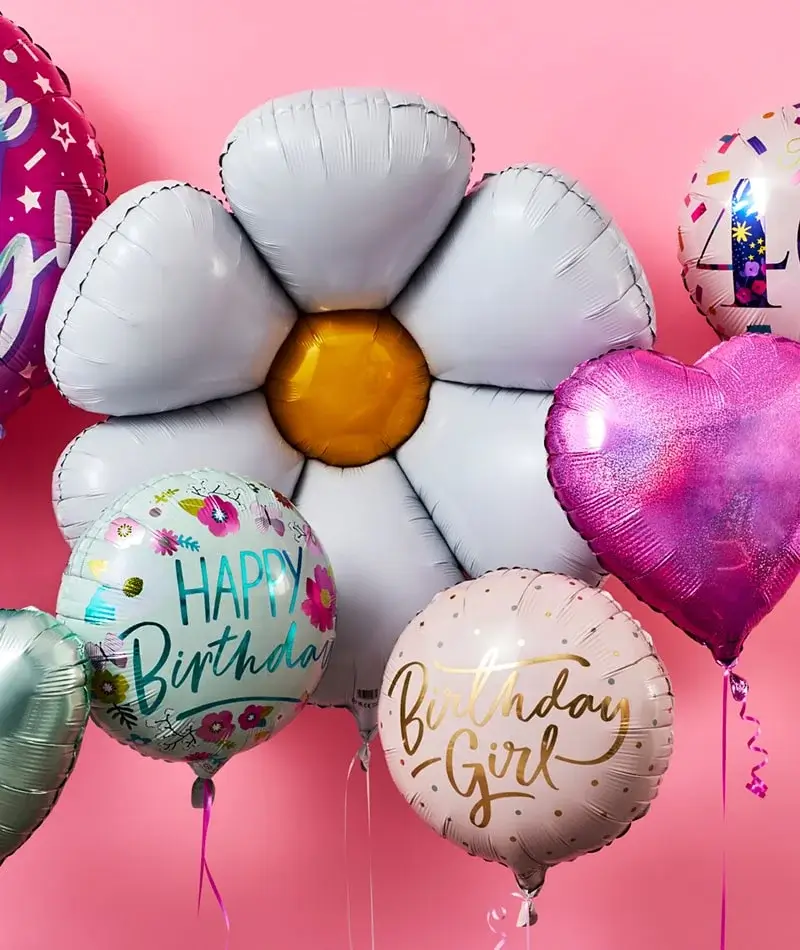 A collection of colorful balloons against a pink background. The central balloon is shaped like a white flower with a yellow center. Surrounding it are round balloons with messages like 'Happy Birthday' and 'Birthday Girl', along with a heart-shaped pink balloon. A collection of colorful balloons against a pink background. The central balloon is shaped like a white flower with a yellow center. Surrounding it are round balloons with messages like 'Happy Birthday' and 'Birthday Girl', along with a heart-shaped pink balloon.