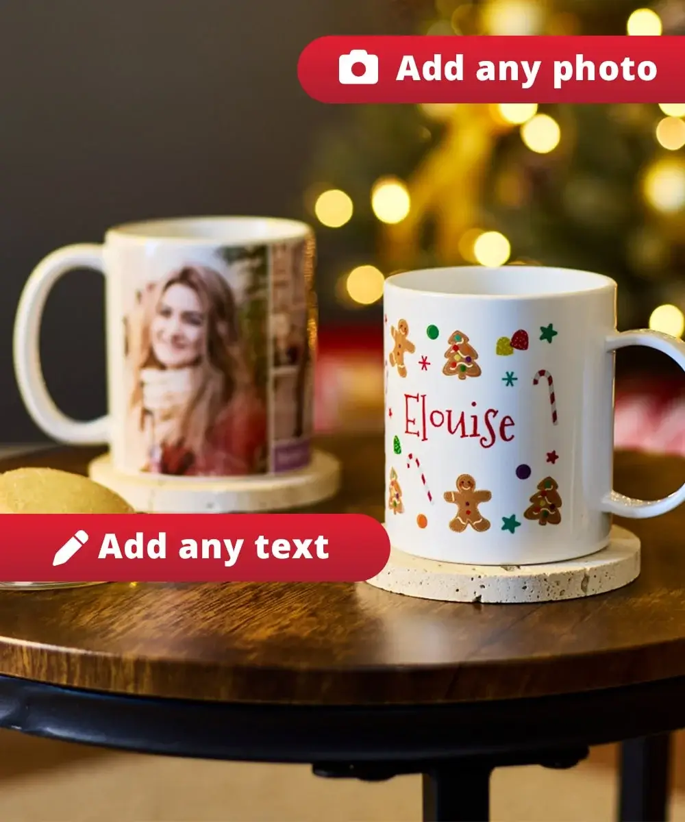 Two personalised mugs on a wooden table, one with a photo and the other decorated with festive gingerbread men, candy canes, stars, and the name Eloise, with blurred Christmas lights in the background and a plate of cookies nearby.