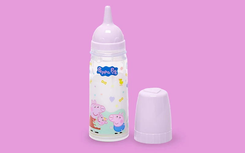 A Peppa Pig baby bottle with a clear body, white cap and soft teat, decorated with Peppa Pig characters and small icons, displayed on a pink background.
