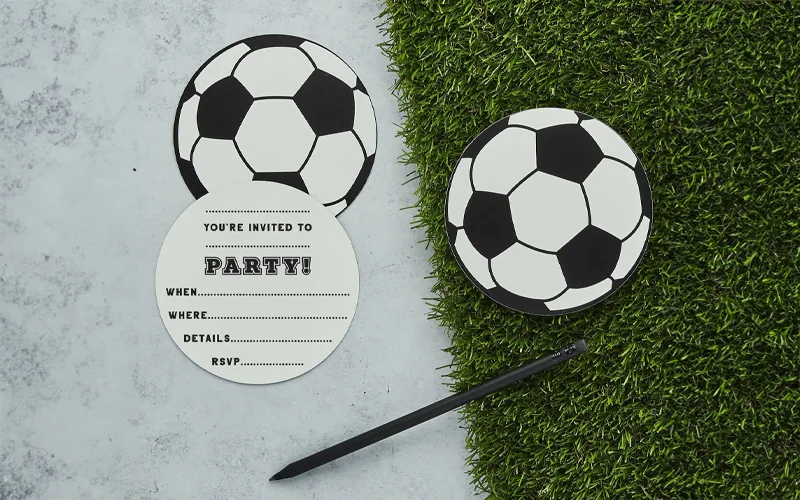 A set of football‑shaped party invitations displayed beside artificial grass, including an opened invitation card with space to fill in party details such as date, time, location and RSVP information, alongside a black pen. A set of football‑shaped party invitations displayed beside artificial grass, including an opened invitation card with space to fill in party details such as date, time, location and RSVP information, alongside a black pen.