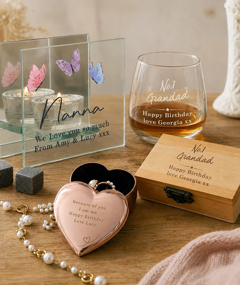 A collection of personalised gifts including an engraved tealight holder, whisky glass, wooden keepsake box and heart-shaped trinket box, displayed on a wooden table.