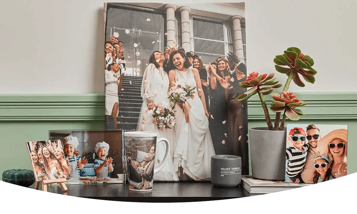 Wedding‑themed photo gifts displayed on a table, including framed prints, a large canvas, a personalised mug, and a small potted plant. Wedding‑themed photo gifts displayed on a table, including framed prints, a large canvas, a personalised mug, and a small potted plant.