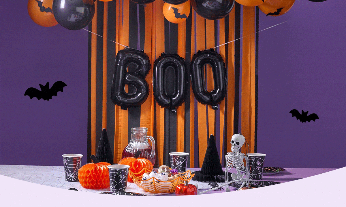 Halloween-themed setup with skulls, pumpkins, spider webs, a personalized mug and candle, candy bowl, and festive decorations against a purple backdrop.