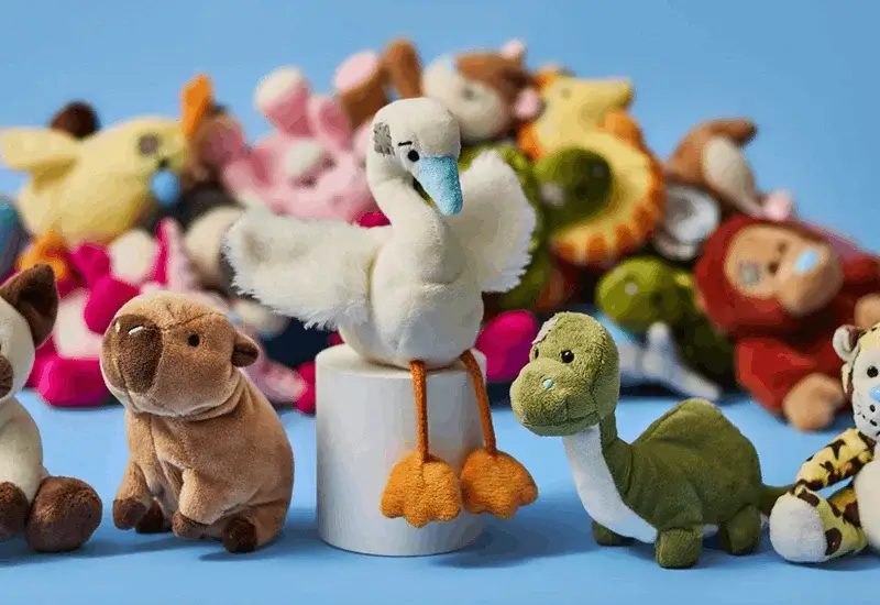Assorted soft toy animals including a swan, dinosaur, pig, and tiger displayed against a blue background with plush toys behind.