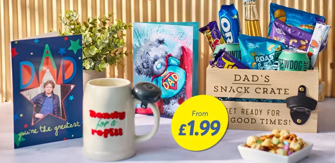 'A display of Father's Day gifts including a card with the text 'DAD you're the greatest', a mug with 'Ready for a refill' written on it, another card with 'Happy Father's Day' text, and a wooden crate labeled 'DAD'S SNACK CRATE GET READY FOR GOOD TIMES!' filled with various snacks. There is also a yellow circle with the text 'From £1.99'