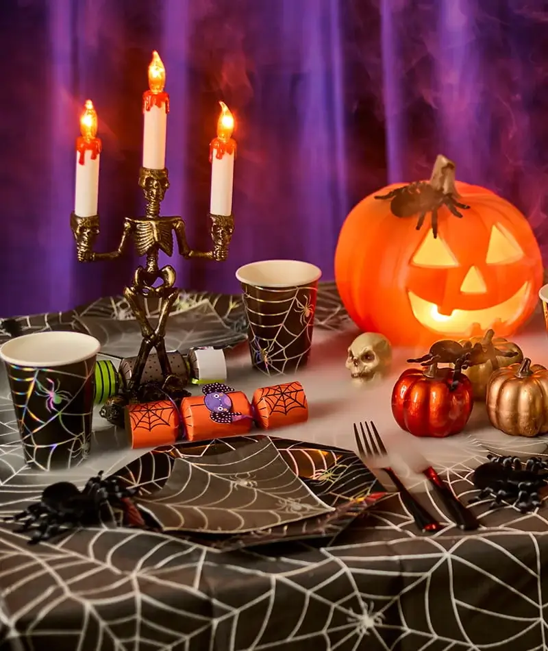 Halloween party table with spiderweb decorations, glowing pumpkin lantern, novelty candles and spooky themed tableware. Halloween party table with spiderweb decorations, glowing pumpkin lantern, novelty candles and spooky themed tableware.