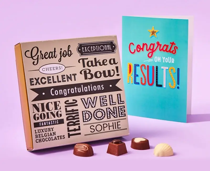 Celebratory arrangement featuring congratulatory cards, a box of chocolates with phrases like 'Great job' and 'Well Done', a graduation card for Joshua, and a balloon that says 'You've PASSED'