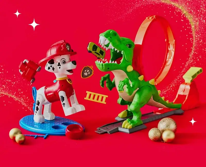Toy Dalmatian firefighter and green dinosaur on a red background with a loop track, flying toy cars, firefighting accessories, and gold Christmas ornaments. Toy Dalmatian firefighter and green dinosaur on a red background with a loop track, flying toy cars, firefighting accessories, and gold Christmas ornaments.
