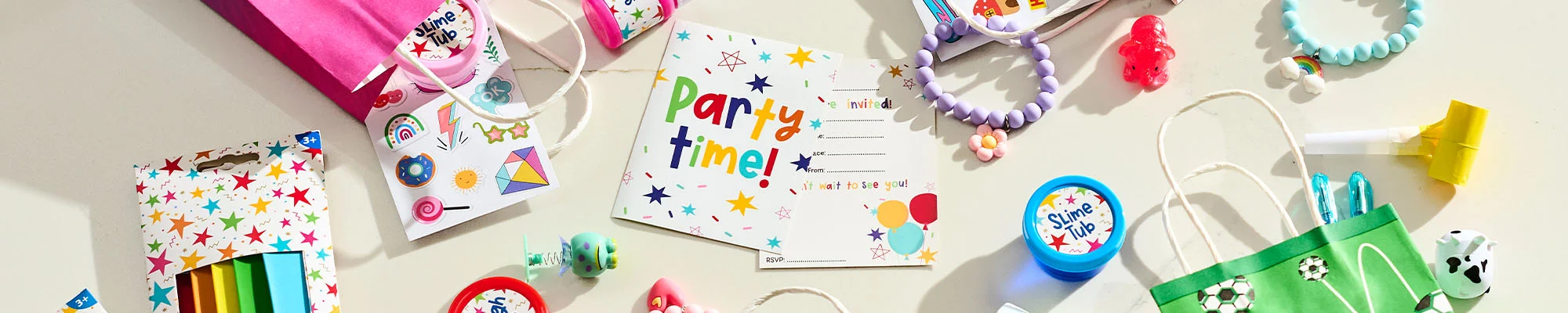 A flat-lay display of children's party game prizes and party bag fillers, featuring a colourful ‘Party Time!’ invitation, sticker sheets, crayons, slime tubs, novelty toys, beaded bracelets, party blowers and gift bags. A football-themed party bag and bright pink favour bag are included among the assorted prizes and accessories arranged on a light background.