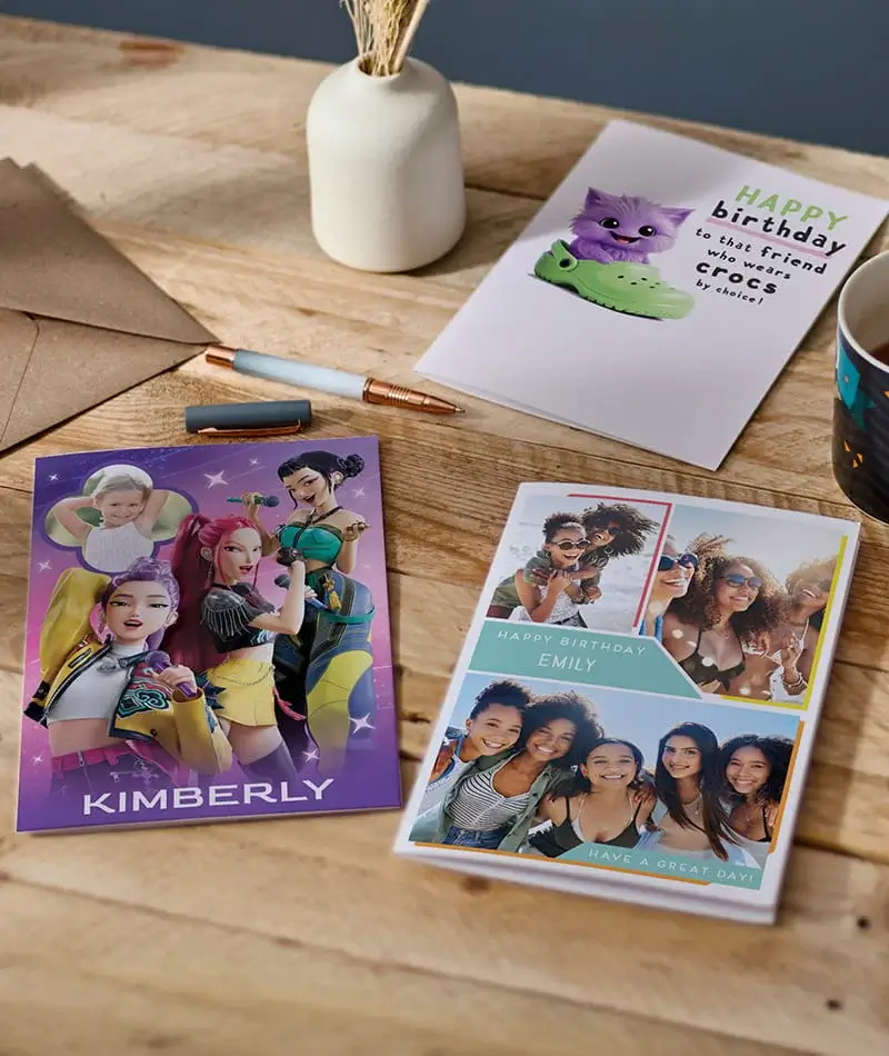 Selection of birthday cards including personalised photo cards, a character-themed card, and a humorous birthday card displayed on a wooden table.
