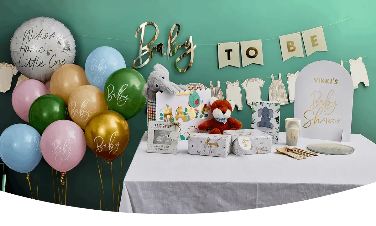 A baby shower table display with gift bags, plush toys, wrapped presents, cups, plates, and gold decorations, surrounded by colorful balloons and a banner reading Baby To Be.
