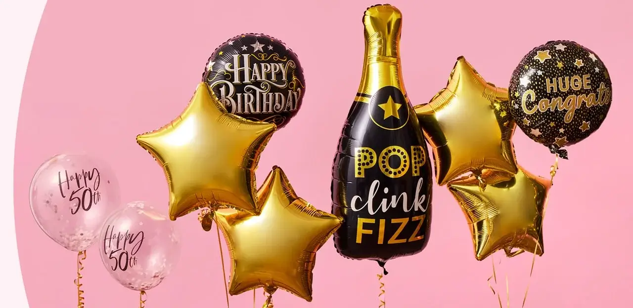 A group of celebratory balloons on a pink background, including gold stars, 'Happy 50th' balloons, and a champagne bottle-shaped balloon with the text 'POP clink FIZZ'