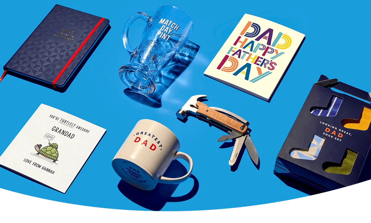 Father’s Day gift selection on blue background including a Dad mug, match day pint glass, greeting cards, multi-tool, notebook, and boxed socks