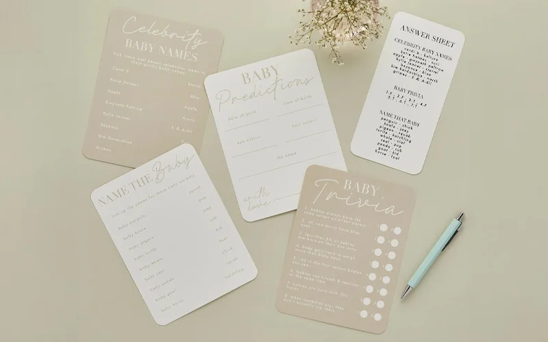 A baby shower greeting card featuring a floral wreath design with gold lettering reading ‘On Your Baby Shower’, displayed on a green background beside a white and gold pen.
