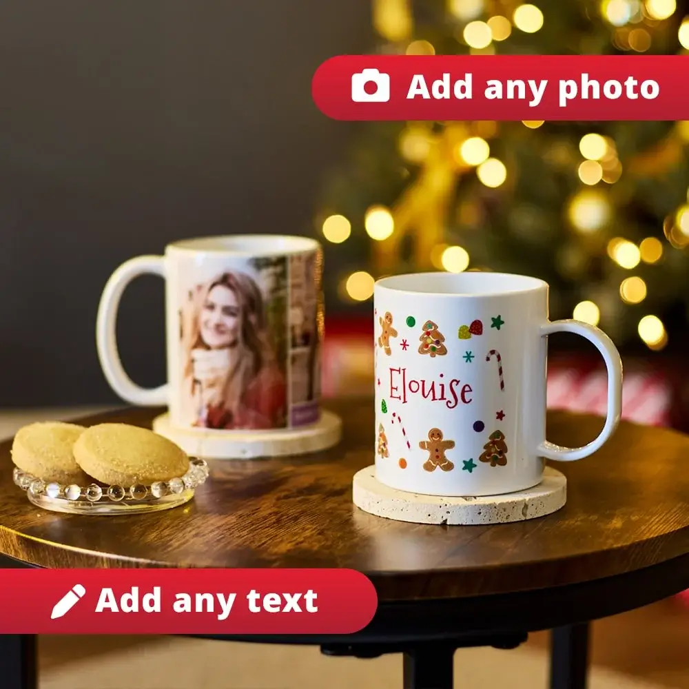 Two personalised mugs on a wooden table, one with a photo and the other decorated with festive gingerbread men, candy canes, stars, and the name Eloise, with blurred Christmas lights in the background and a plate of cookies nearby.