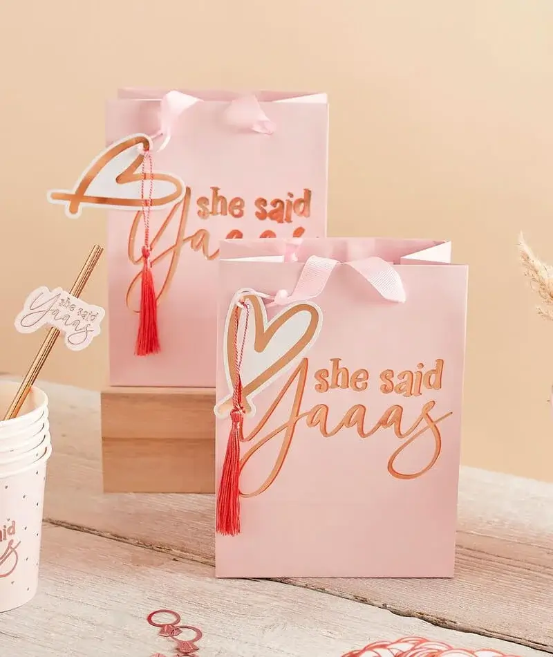 A bridal celebration setup with gold and white balloons, a large personalised balloon, a pink table with drinks, a disco ball and dried flowers against soft pink decorations.