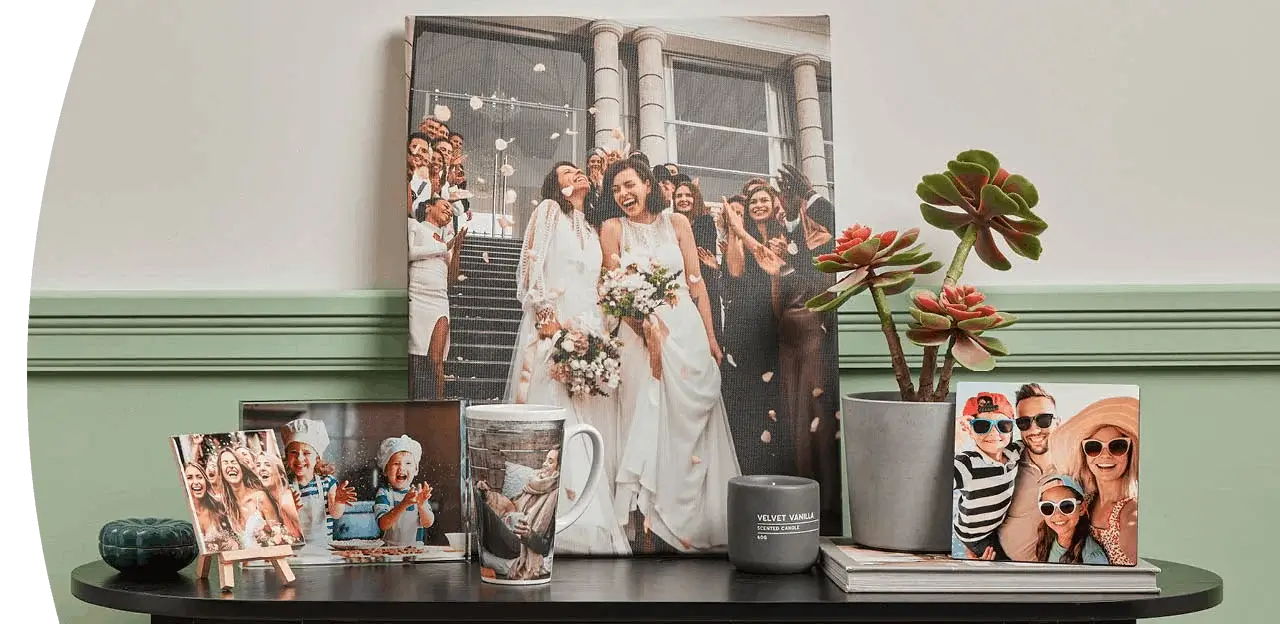 Wedding‑themed photo gifts displayed on a table, including framed prints, a large canvas, a personalised mug, and a small potted plant. Wedding‑themed photo gifts displayed on a table, including framed prints, a large canvas, a personalised mug, and a small potted plant.
