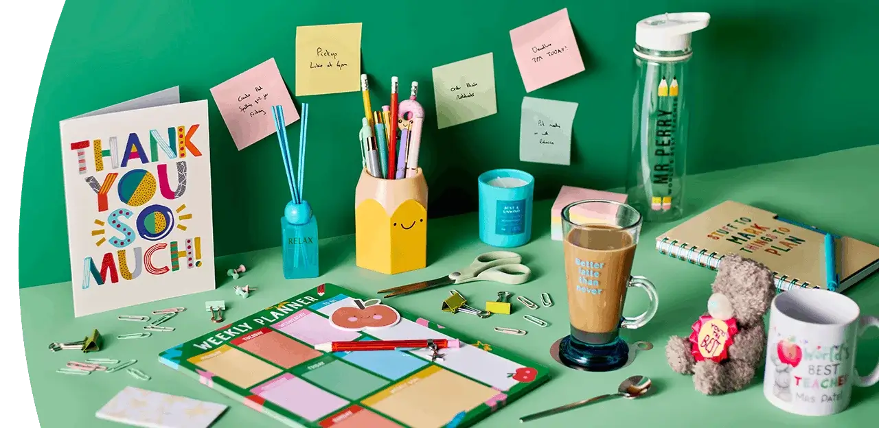 Teacher appreciation setup with thank you card, planner, stationery, mug, water bottle, and small gifts arranged on a green background