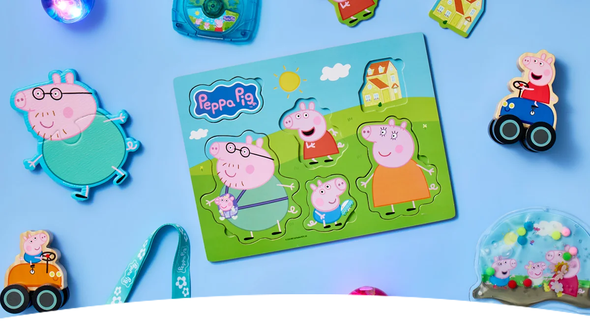 A selection of Peppa Pig children’s toys arranged on a light blue background, centred around a colourful Peppa Pig wooden puzzle featuring Peppa and family characters, with small toys and accessories scattered around.
