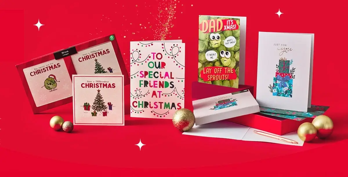 A festive display of Christmas cards arranged on a bright red background, featuring various designs such as a decorated Christmas tree, colorful gift boxes, and playful text like “To Our Special Friends at Christmas” and “Dad It’s Xmas! Lay Off the Sprouts!” Gold ornaments are placed around the cards for decoration. A festive display of Christmas cards arranged on a bright red background, featuring various designs such as a decorated Christmas tree, colorful gift boxes, and playful text like “To Our Special Friends at Christmas” and “Dad It’s Xmas! Lay Off the Sprouts!” Gold ornaments are placed around the cards for decoration.