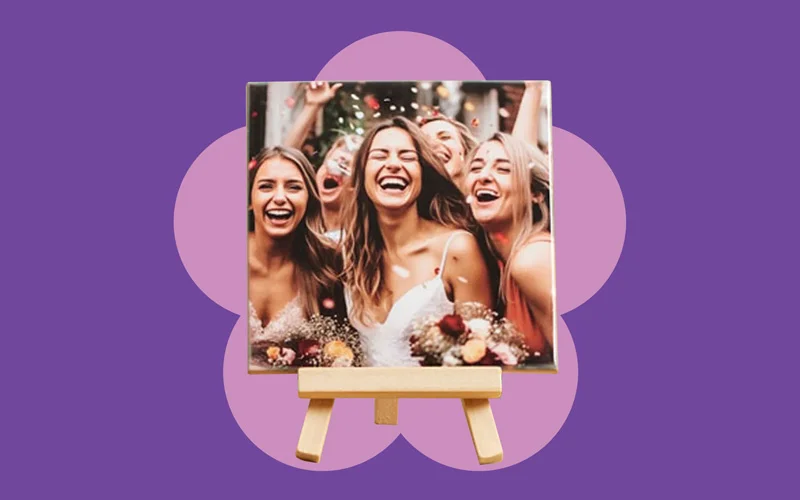 A square photo tile displayed on a small wooden easel, shown against a purple background with a pink flower shape.