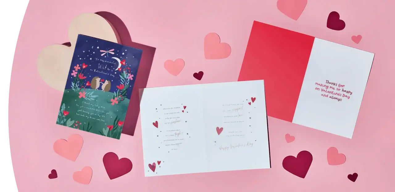 A flat‑lay of Valentine’s Day greeting cards on a pink background, surrounded by scattered paper hearts in various shades of pink and red.