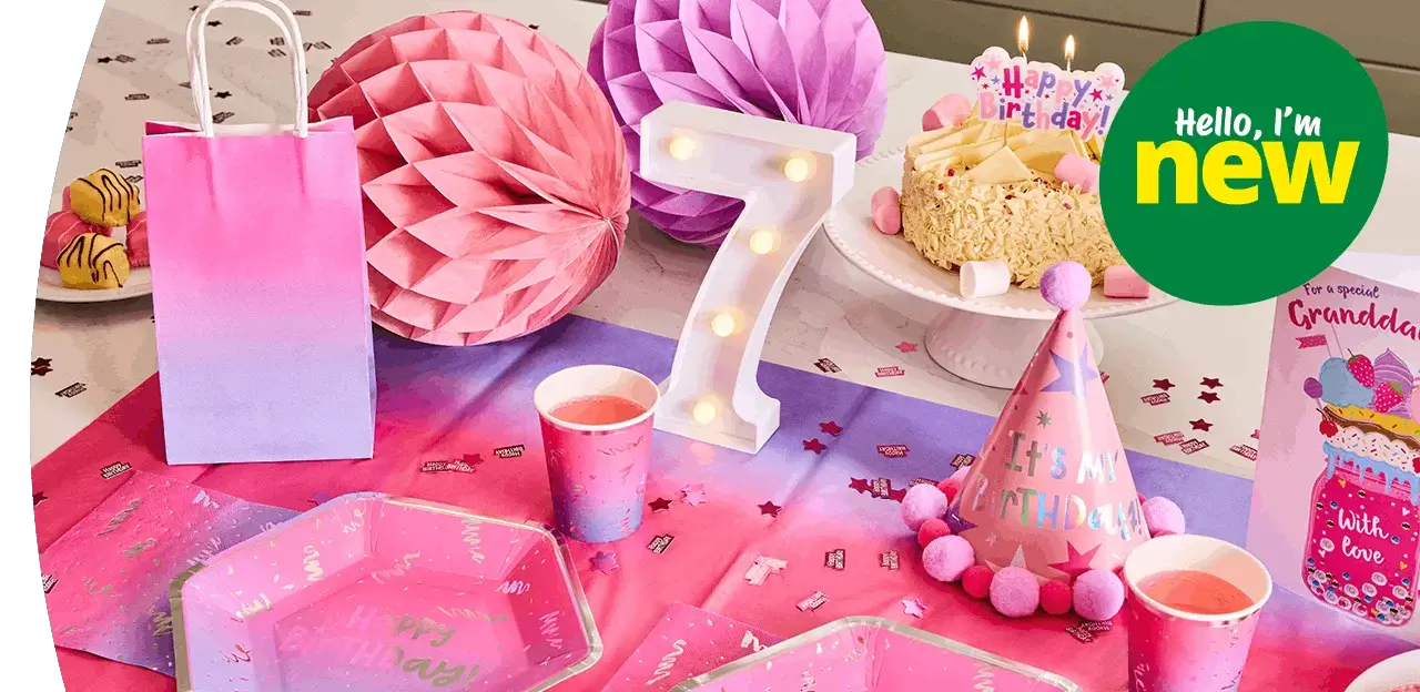 Pink and purple birthday party table setup with a lit number 7 decoration, birthday cake, gift bag, party hat, cups, plates, and festive paper decorations on a colorful tablecloth. Pink and purple birthday party table setup with a lit number 7 decoration, birthday cake, gift bag, party hat, cups, plates, and festive paper decorations on a colorful tablecloth.