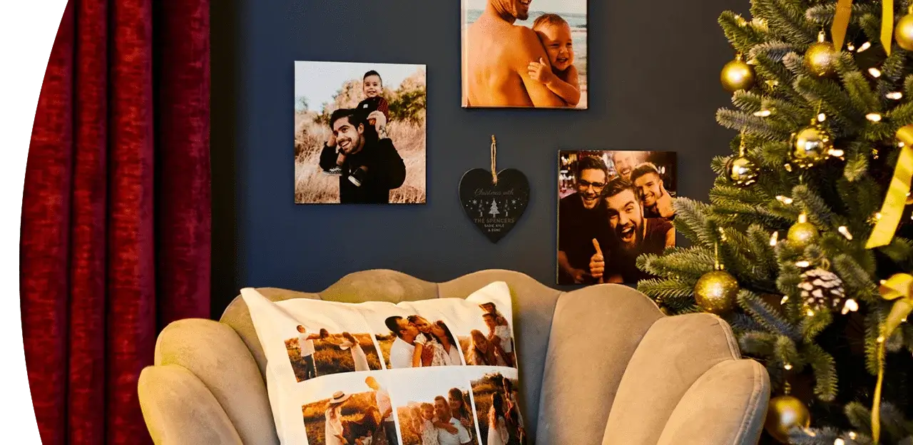 A cozy living room decorated for Christmas with a beige armchair featuring a photo collage pillow, a dark wall displaying several photo prints, and a Christmas tree adorned with gold ornaments and ribbons next to red curtains. A cozy living room decorated for Christmas with a beige armchair featuring a photo collage pillow, a dark wall displaying several photo prints, and a Christmas tree adorned with gold ornaments and ribbons next to red curtains.