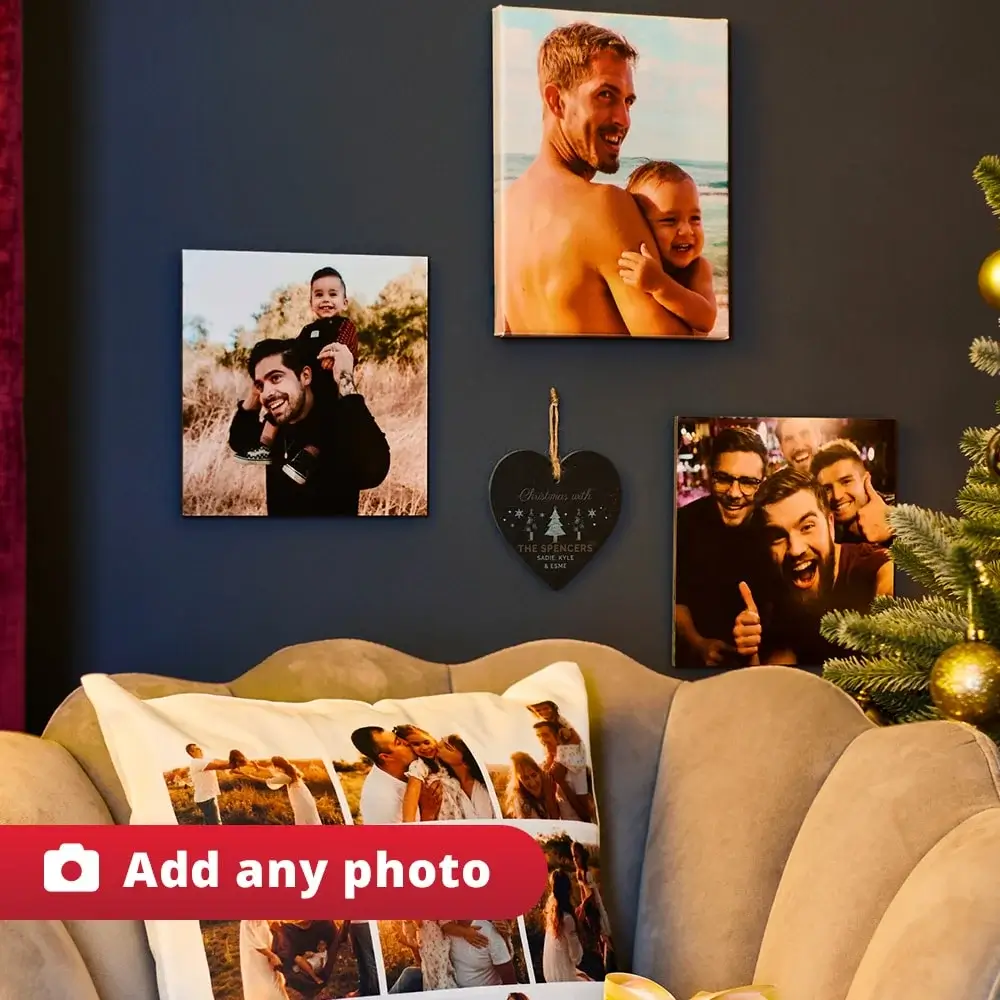 Cozy living room with a photo collage pillow on a beige armchair, framed family photos on a dark blue wall, heart-shaped Christmas ornament, and a partially visible decorated Christmas tree. Cozy living room with a photo collage pillow on a beige armchair, framed family photos on a dark blue wall, heart-shaped Christmas ornament, and a partially visible decorated Christmas tree.