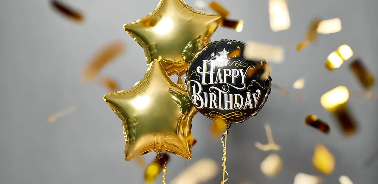 Happy Birthday balloon bouquet featuring a black birthday message balloon, gold star-shaped balloons, and falling gold confetti.
