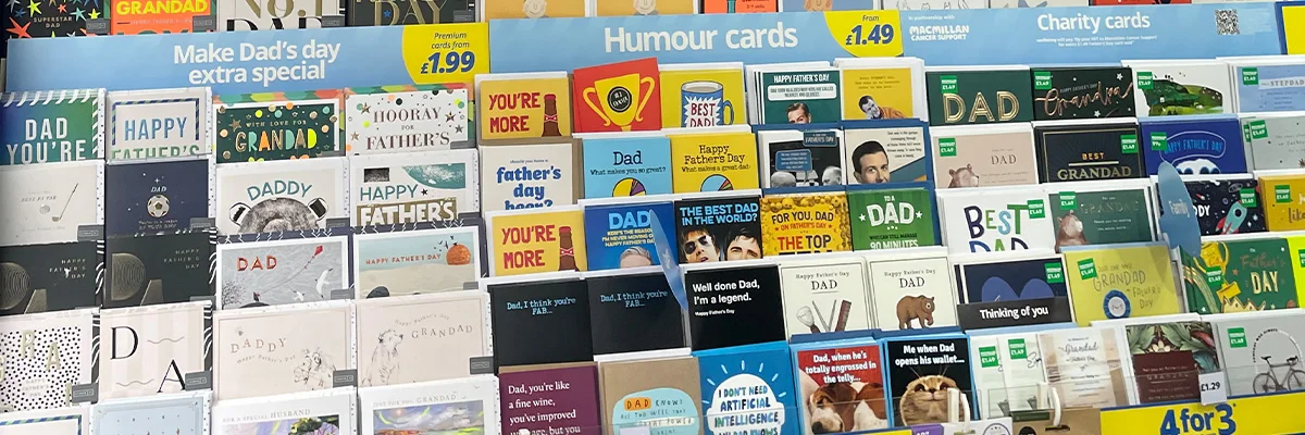 A wide in‑store display of Father’s Day greeting cards arranged across multiple shelves, with sections labelled ‘Make Dad’s day extra special,’ ‘Humour cards,’ and ‘Charity cards,’ featuring a variety of designs for Dad, Grandad and other family members, with price signage and a ‘4 for 3’ offer shown at the bottom. A wide in‑store display of Father’s Day greeting cards arranged across multiple shelves, with sections labelled ‘Make Dad’s day extra special,’ ‘Humour cards,’ and ‘Charity cards,’ featuring a variety of designs for Dad, Grandad and other family members, with price signage and a ‘4 for 3’ offer shown at the bottom.