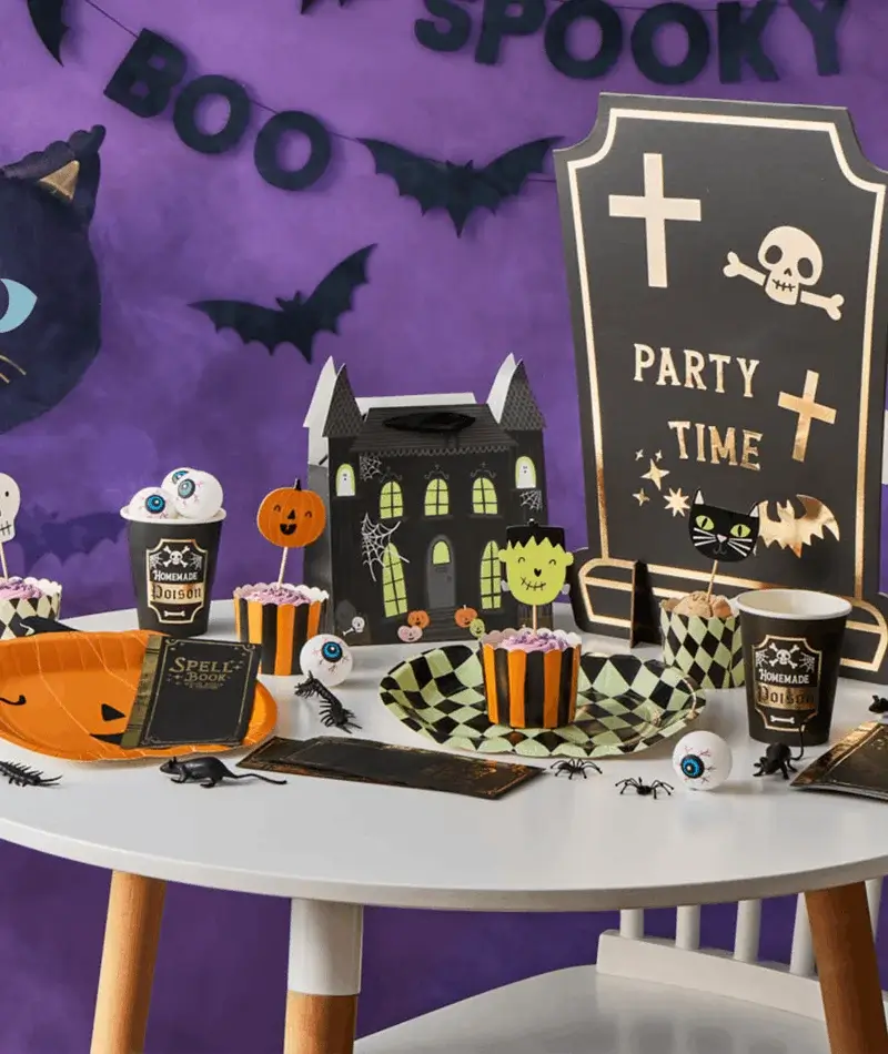 Halloween party table with spooky tableware, haunted house decoration, eyeball cupcakes, bats, spiders, and a Party Time tombstone backdrop. Halloween party table with spooky tableware, haunted house decoration, eyeball cupcakes, bats, spiders, and a Party Time tombstone backdrop.