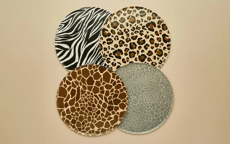 A set of four round party plates featuring animal-inspired patterns, including zebra stripes, leopard print, giraffe markings and a grey textured design. The plates are displayed overlapping against a neutral beige background as part of a safari-themed party collection. A set of four round party plates featuring animal-inspired patterns, including zebra stripes, leopard print, giraffe markings and a grey textured design. The plates are displayed overlapping against a neutral beige background as part of a safari-themed party collection.