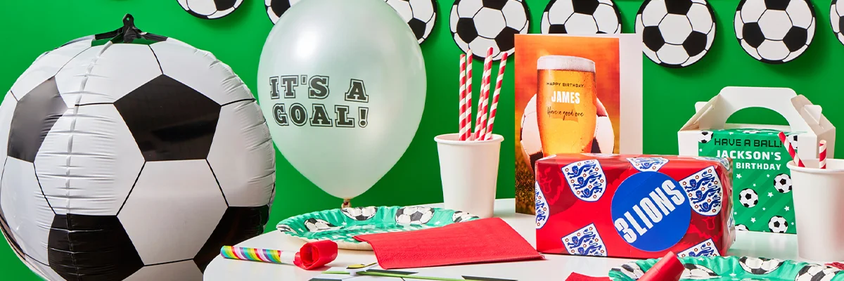 A football-themed party table display featuring a large football balloon, an ‘It’s a Goal!’ printed balloon, football-print plates and napkins, striped paper straws, party blowers, a personalised birthday card, and football-themed party favour boxes and gift bags arranged against a bright green backdrop. A football-themed party table display featuring a large football balloon, an ‘It’s a Goal!’ printed balloon, football-print plates and napkins, striped paper straws, party blowers, a personalised birthday card, and football-themed party favour boxes and gift bags arranged against a bright green backdrop.