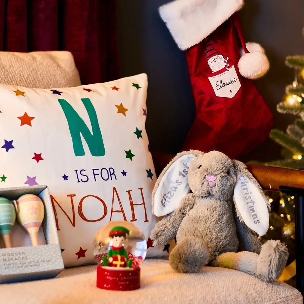 Cozy Christmas scene with a personalized Noah pillow, Eloise stocking, plush bunny with First Christmas embroidery, elf snow globe, and pastel wooden maracas in a box. Cozy Christmas scene with a personalized Noah pillow, Eloise stocking, plush bunny with First Christmas embroidery, elf snow globe, and pastel wooden maracas in a box.
