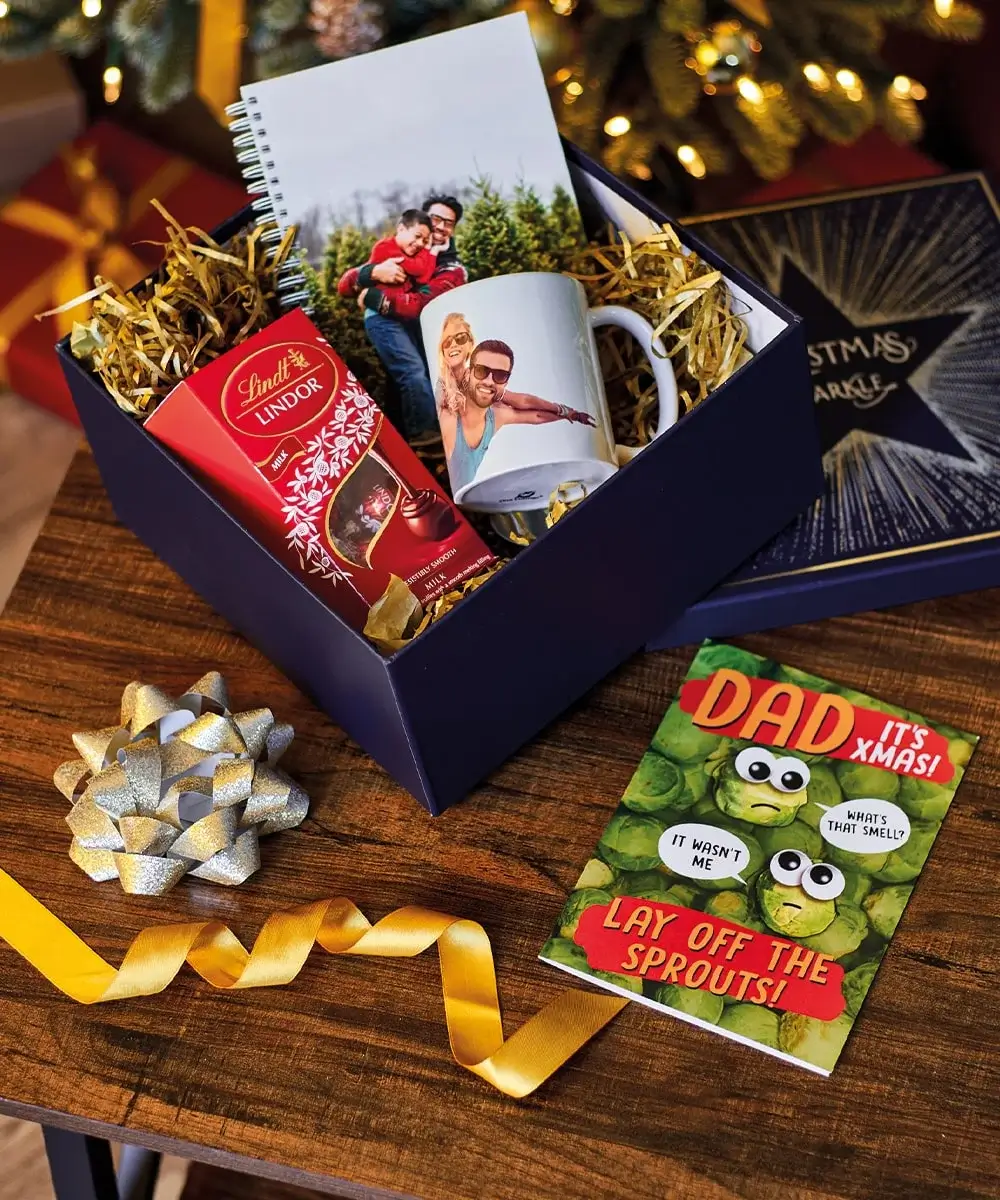 Christmas gift set for him featuring a navy box with Lindt chocolates, a photo mug, a personalized notebook, and a humorous card reading 'DAD IT'S XMAS! LAY OFF THE SPROUTS!' with cartoon sprouts and speech bubbles.