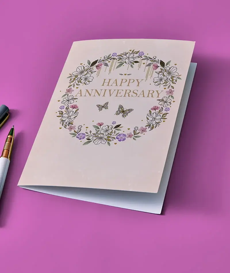 Floral Happy Anniversary greeting card with gold lettering and delicate flower wreath design on a pink background Floral Happy Anniversary greeting card with gold lettering and delicate flower wreath design on a pink background