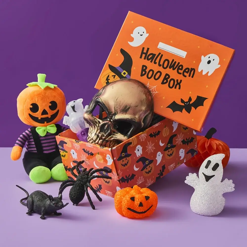 A Halloween display with a haunted house treat box filled with cupcakes and eyeball candies, surrounded by themed cups, napkins, and decorations on a purple background