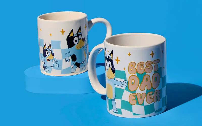 Two ceramic mugs featuring Bluey character illustrations on a blue background, one showing Bluey and family characters and the other printed with bold text reading ‘Best Dad Ever’ alongside a checkerboard pattern. Two ceramic mugs featuring Bluey character illustrations on a blue background, one showing Bluey and family characters and the other printed with bold text reading ‘Best Dad Ever’ alongside a checkerboard pattern.