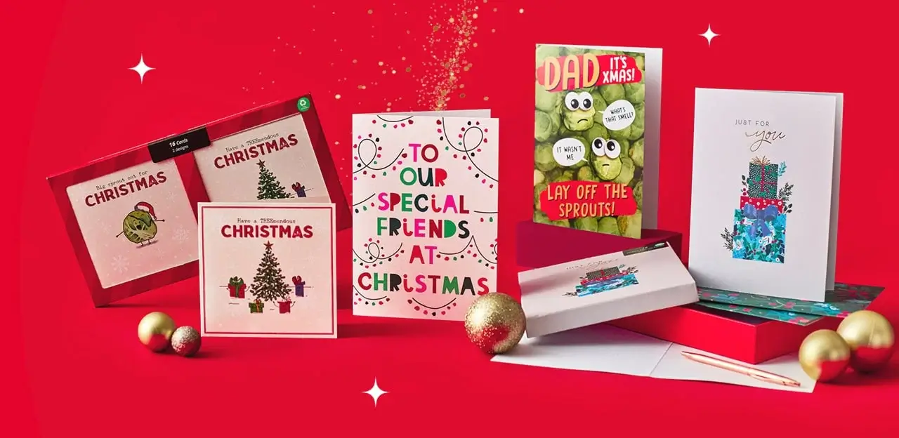 A festive display of Christmas cards arranged on a bright red background, featuring various designs such as a decorated Christmas tree, colorful gift boxes, and playful text like “To Our Special Friends at Christmas” and “Dad It’s Xmas! Lay Off the Sprouts!” Gold ornaments are placed around the cards for decoration. A festive display of Christmas cards arranged on a bright red background, featuring various designs such as a decorated Christmas tree, colorful gift boxes, and playful text like “To Our Special Friends at Christmas” and “Dad It’s Xmas! Lay Off the Sprouts!” Gold ornaments are placed around the cards for decoration.