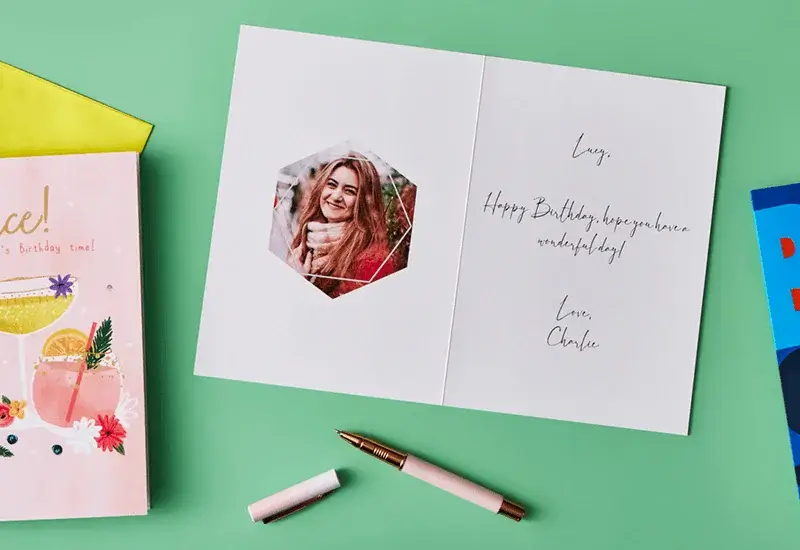 Open personalised birthday card with a printed photo, handwritten birthday message, and pen displayed on a green background.
