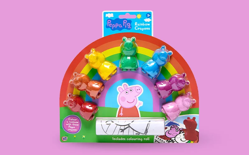 A Peppa Pig rainbow crayon set featuring pig‑shaped crayons arranged in a rainbow display, with a colouring roll included, shown on a pink background.