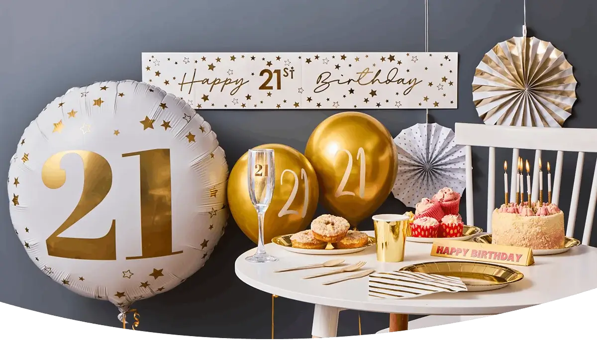 Gold and white 21st birthday setup with large balloons, a decorated cake with candles, cupcakes, party tableware, and a festive banner. Gold and white 21st birthday setup with large balloons, a decorated cake with candles, cupcakes, party tableware, and a festive banner.