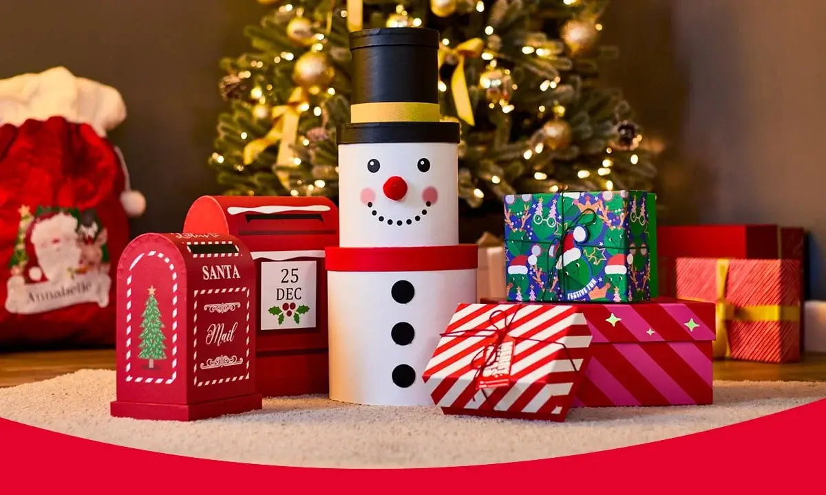 Christmas-themed display with a snowman-shaped gift box, red Santa Mail boxes, and wrapped presents in front of a decorated tree.