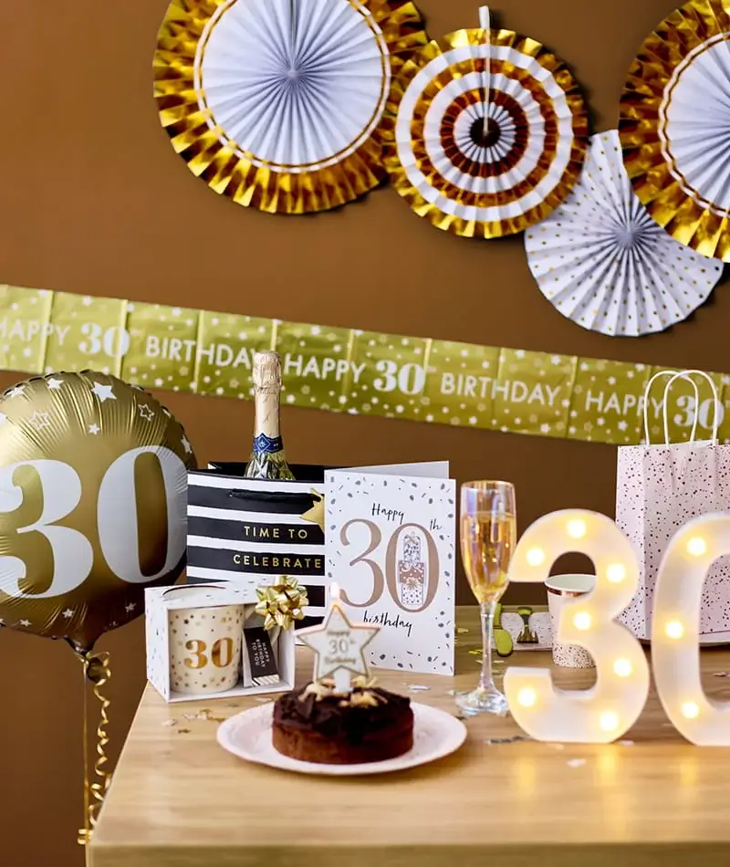 30th birthday celebration display featuring a gold number balloon, birthday card, cake, champagne, party decorations and illuminated number lights. 30th birthday celebration display featuring a gold number balloon, birthday card, cake, champagne, party decorations and illuminated number lights.